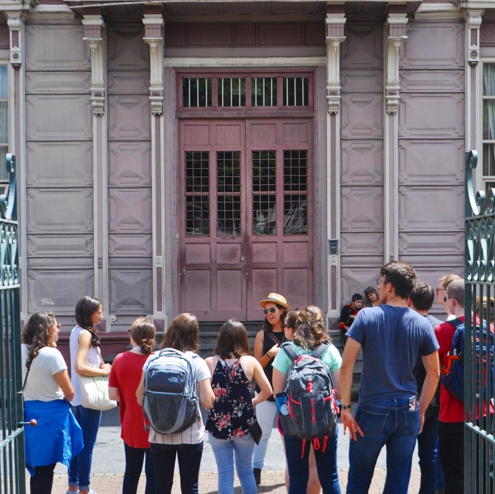 A group of Northeastern University students stop by Escuela Metálica, a landmark building of downtown San José known for its French design and unusual lilac color.